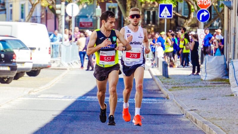 Two male runners competing intensely in a city marathon event on a sunny day.